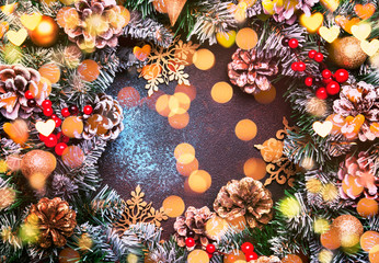 Christmas or New Year frame composition with  green snow fir branches, pine cones, golden snowflakes, Christmas balls, red berries, and alarm clock on brown background, top view