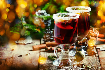 Christmas and New Year festive drink, hot mulled wine with cinnamon, cardamom, orange and anise star on background of green spruce branches and lights, rustic wooden table, selective focus