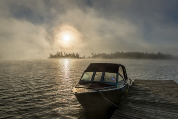 Boat at dock at sunrise on misty morning in the Georgian Bay, Ontario, Canada, with islands in...