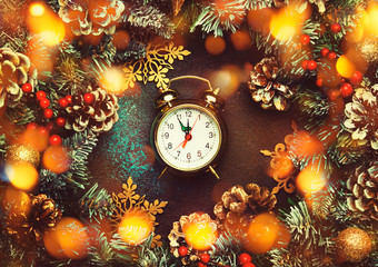 Fototapeta na wymiar Christmas or New Year frame composition with green snow fir branches, pine cones, golden snowflakes, Christmas balls, red berries, and alarm clock on brown background, top view