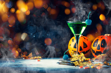 Halloween composition with festive drink, green cocktail and pumpkins lanterns, smoke and fallen leaves on night dark blue background, selective focus - Powered by Adobe