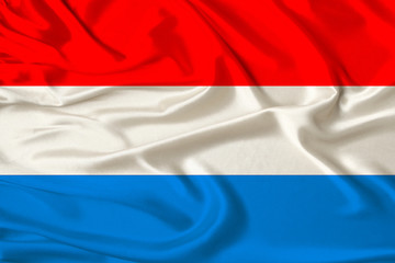 beautiful photo of the Luxembourg national flag on delicate shiny silk with soft draperies, the concept of state power, country life, horizontal, close-up, copy space