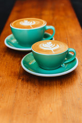 Two cups of cappuccino with latte art on wooden background.