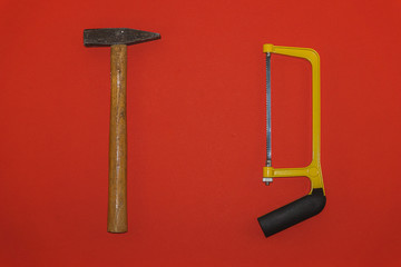Old metal hammer and saw on red background