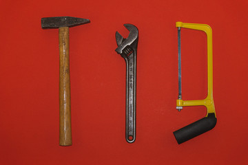 Metal hammer, wrench, and saw on red background
