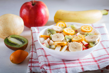 Vegetarian salad of bananas, apples, pears, kumquats and kiwi on linen tablecloth, close up, selective focus.