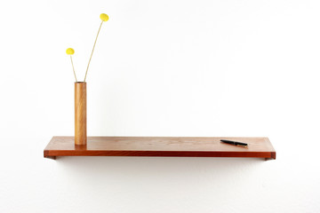 midcentury teak shelf on white wall in the living room with a wooden vase and a plack pen on it next to it a space age vintage orange lamp danish design front side low angle high view HIGH RESOLUTION