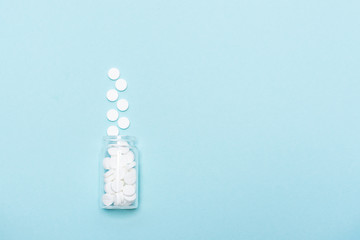 Big white medicine pills in glass bottle on blue background with copy space for your design. Flu season concept. Template for medicine blog social media.