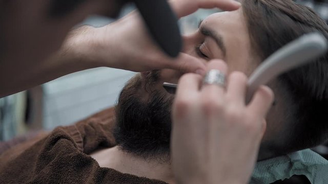 Barber shaves men with a long beard with straight razor blade in s hair salon or barbershop. Man's haircut and shaving at the hairdresser, barber shop and shaving salon.