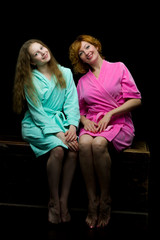 Fototapeta na wymiar Daughter and mother in bathrobes posing in the studio. The conce