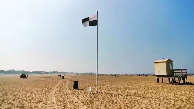 The beach of vrouwenpolder with a black and white checkered flag waving in the wind, water sports allowed sign, touristic coastal village in zeeland, The netherlands