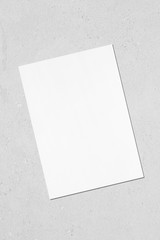 Empty white vertical rectangle poster mockup with soft shadow lying diagonally on neutral light grey concrete background. Flat lay, top view