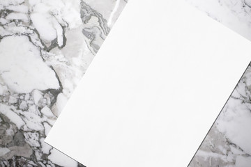 Close up of empty white rectangle poster mockup lying diagonally with soft shadow on grey marble background. Flat lay, top view. Open composition.