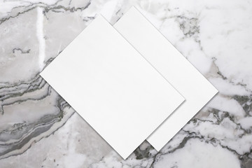 Two empty white rectangle poster mockups lying diagonally on top of each other with soft shadows on neutral light grey marble background. Flat lay, top view