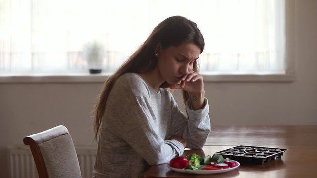Girl sitting at table makes decision eat candies or vegetables