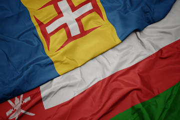 waving colorful flag of oman and national flag of madeira.