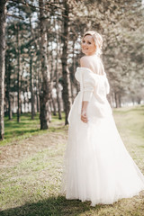 Fototapeta na wymiar Beautiful blonde bride with stylish make-up in white dress in spring garden 