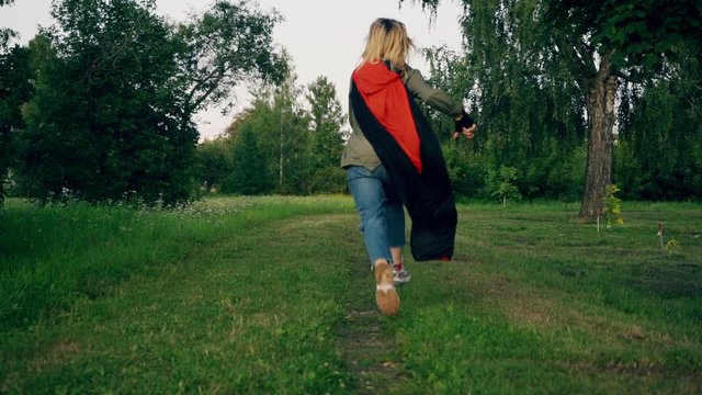 A young girl runs in a park in a red cloak. A young girl in a park in a red cloak. Steadicam slow motion footage.