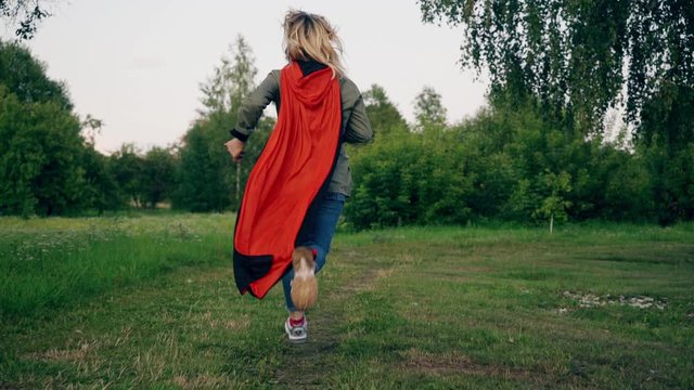 A young girl runs in a park in a red cloak. A young girl in a park in a red cloak. Steadicam slow motion footage.