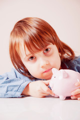 Humorous portrait of cute little child girl save money in piggy bank