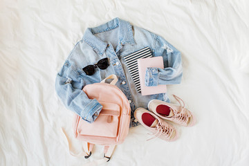 Fototapeta na wymiar Blue jean jacket pale pink with backpack, book and sneakers on white. Women's stylish autumn or spring outfit. Trendy clothes for college. Back to school concept. Flat lay, top view.
