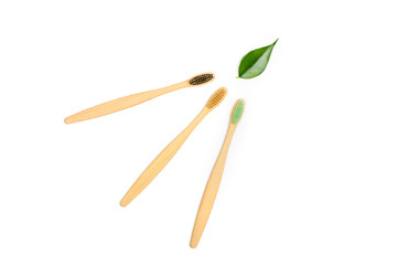 Set of three natural wood bamboo toothbrushes with green leaf on white background. Plastic free concept.