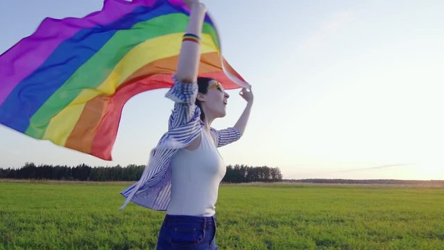 Young attractive woman runs across field with LGBT flag slow mo