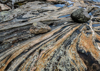 Boulders lying on slab of multi-banded gneiss along the shore of an island in the 30,000-island...