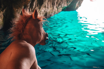 an astonished horse man looks to the fishes swimming in the blue water inside a natural cave