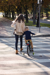Mom is helping the son on bicycle to cross the road at a pedestrian crossing