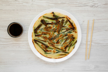 Homemade korean Pajeon scallion pancake on a white plate on a white wooden background, top view. Asian food. Flat lay, overhead, from above.