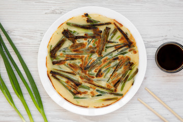 Homemade korean Pajeon scallion pancake on a white plate on a white wooden surface, overhead view. Asian food. Flat lay, top view, from above.