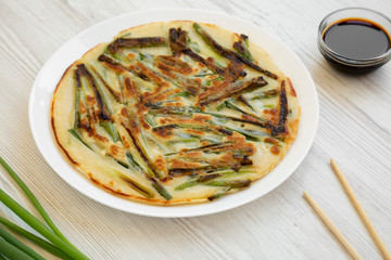 Homemade korean Pajeon scallion pancake on a white plate on a white wooden background, side view. Asian food. Close-up.