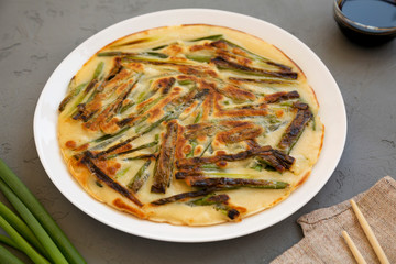 Homemade korean Pajeon scallion pancake on a white plate on a gray background, side view. Asian food. Close-up.