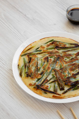 Homemade korean Pajeon scallion pancake on a white plate on a white wooden surface, side view. Asian food. Copy space.