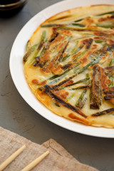 Homemade korean Pajeon scallion pancake on a white plate on a gray background, side view. Asian food. Close-up.
