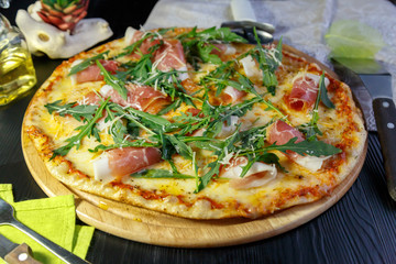 Pizza with bacon, cheese and herbs on a wooden dish on a black wooden background