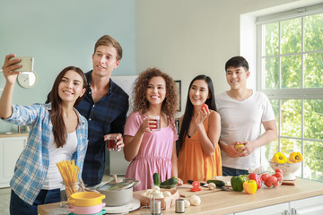 Happy friends taking selfie while cooking together in kitchen