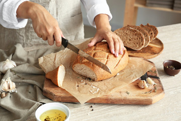 Woman cutting fresh bread in kitchen, closeup