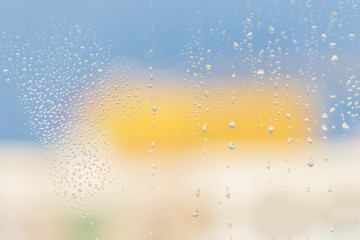 Raindrops on window glass. Blue yellow light background
