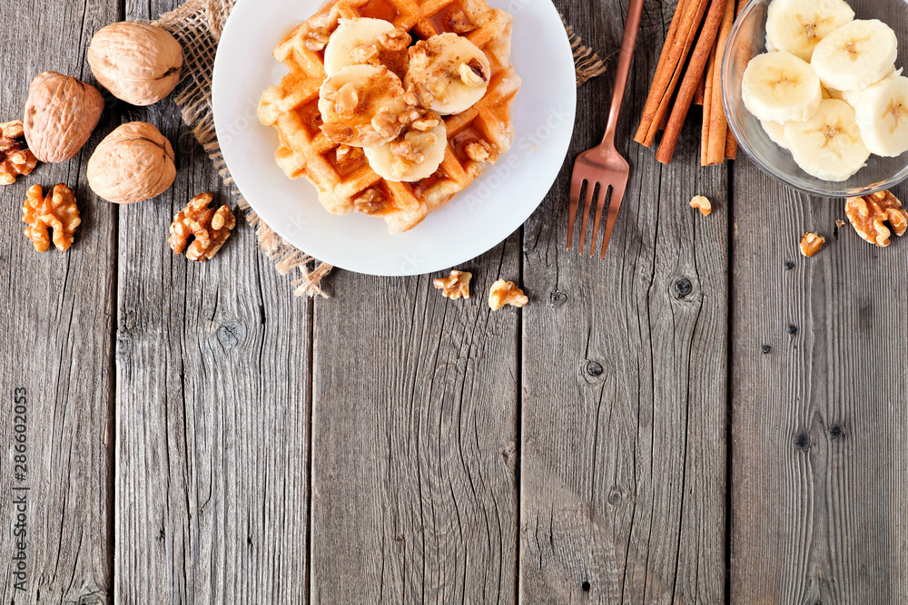 Poster breakfast waffle with bananas, walnuts and syrup. above view top border with copy space over a wood 