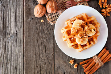 Breakfast waffle with bananas, walnuts and syrup. Top view corner border with copy space over a wood background.