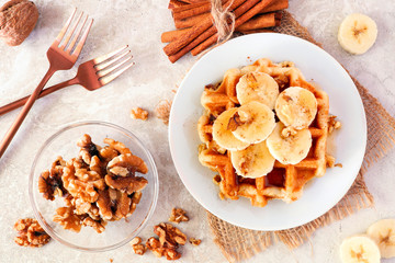 Breakfast waffle with bananas, walnuts and syrup. Top view table scene over a bright background.