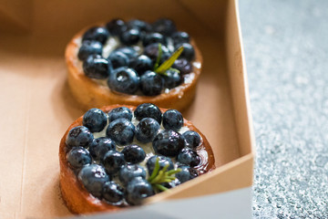 Tartalets with fresh berries in a cardboard box on a grey surface. 
