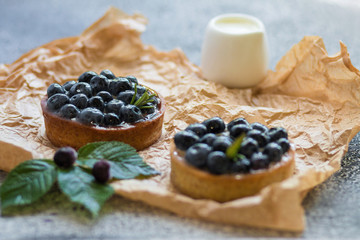 Tartalets with fresh berries on rumpled paper on a grey surface. 