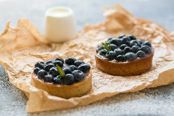Tartalets with fresh berries on rumpled paper on a grey surface. 