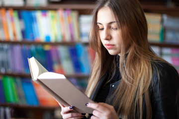 Beautiful teenager schoolgirl reading a book in the library