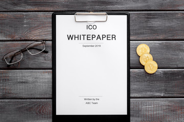 White paper ICO, coins, glasses on gray wooden background top view