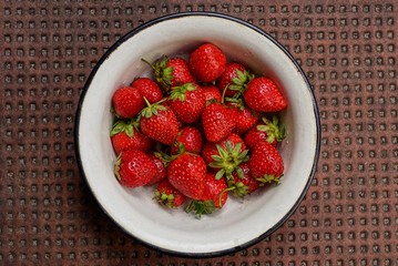 red ripe strawberries in a white metal plate stands on a brown table