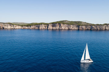 Yacht sailing on the Adriatic sea, cliffs of National park Telascica in background, Croatia